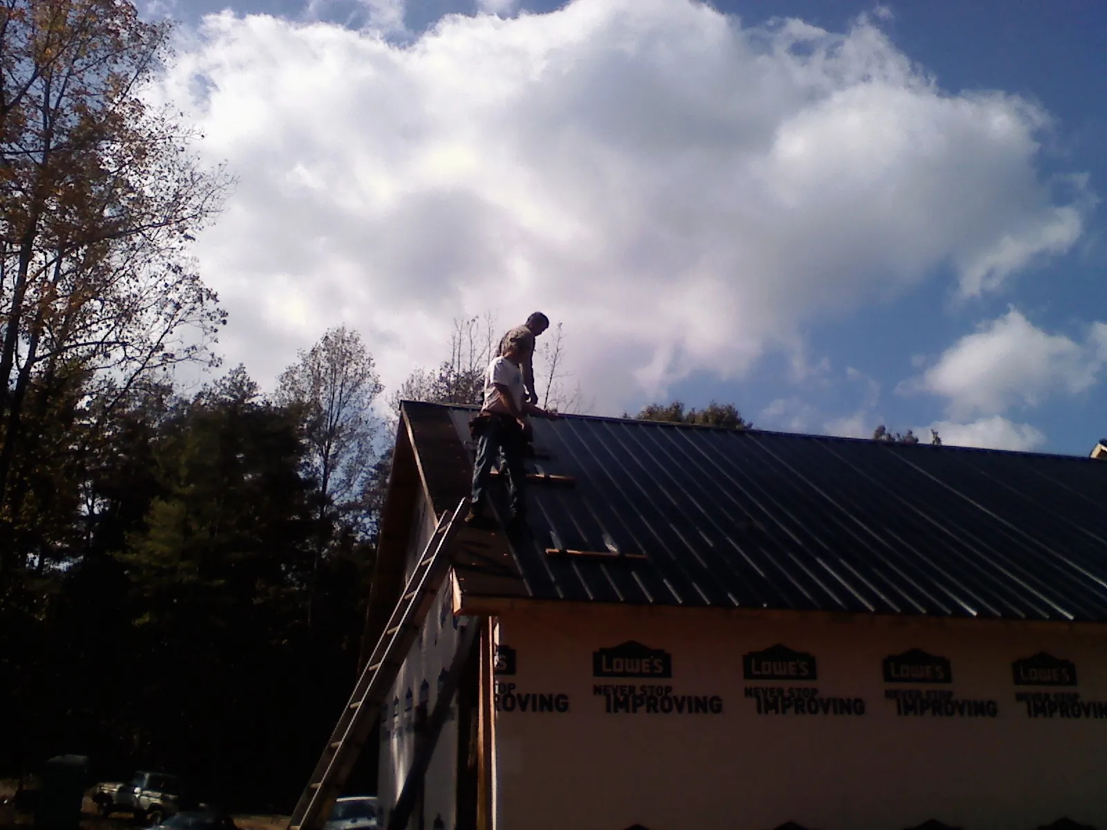 Roofer fastening dark metal panels high against a cloudy sky, from a Roof Inspection job in Elizabeth